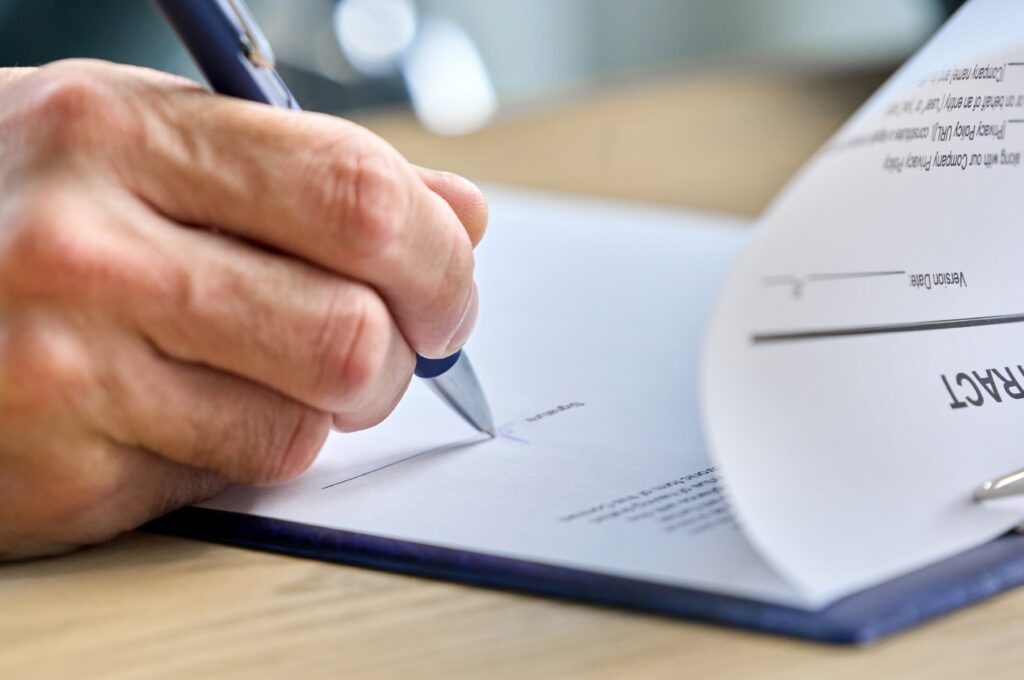 A close-up of a hand using a pen to sign a contract.